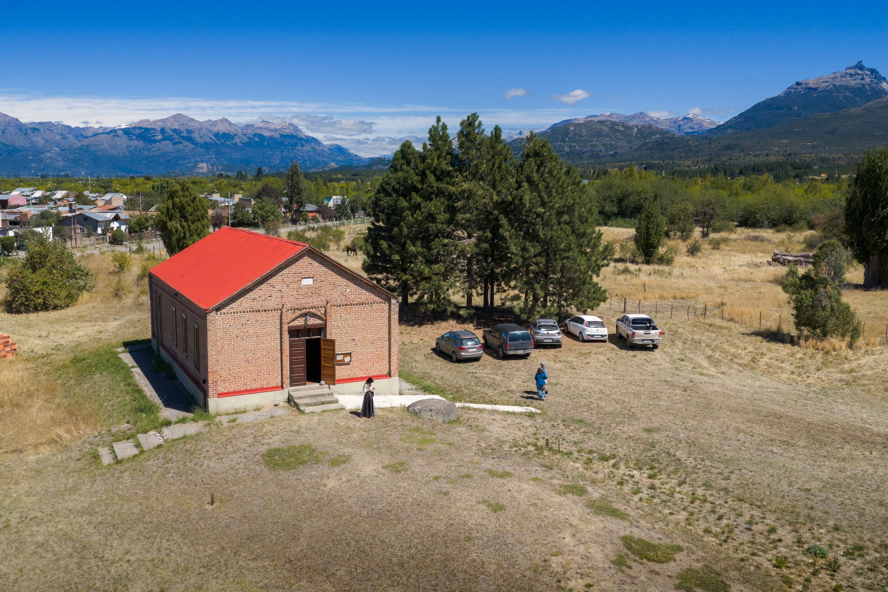 Capilla galesa de ladrillo con techo rojo y la cordillera nevada de fondo en Trevelin